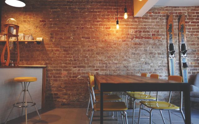 Empty cafe with a brick wall, a timber table and yellow chairs