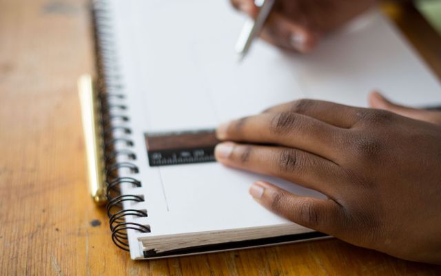 Hand drawing a line in a spiral notebook on a timber desk
