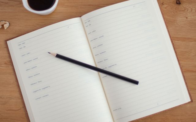 Open notebook with a pencil and a cup of coffee on a timber table